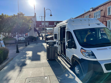 White campervan RV rental parked on a sunny Monterey street. Door open, historic buildings line the background.