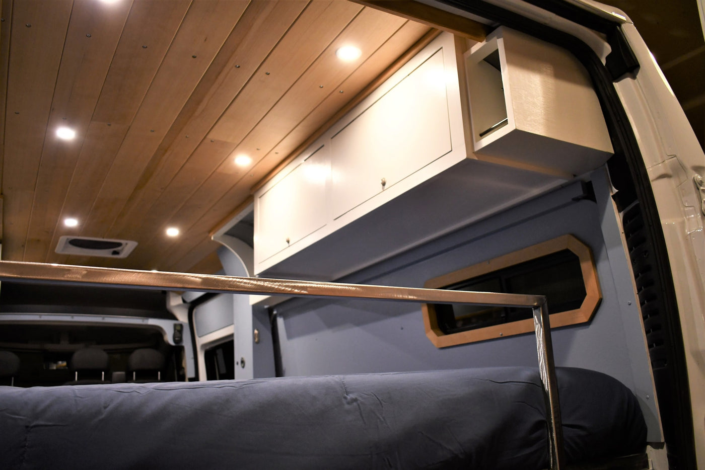 Spacious RV rental interior featuring a wood plank ceiling, bright lights, overhead cabinets, and a comfortable bed. — photo 14