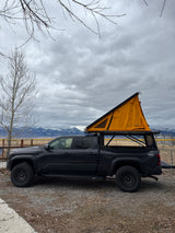 Dark grey Toyota Tacoma overland truck with orange rooftop tent. Great for camping, an alternative to an RV rental adventure.