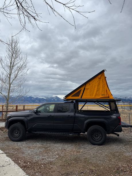 Dark grey Toyota Tacoma overland truck with orange rooftop tent. Great for camping, an alternative to an RV rental adventure.