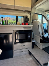 This RV rental kitchen features a microwave, fridge, coffee maker, and a scenic mountain view from the window.
