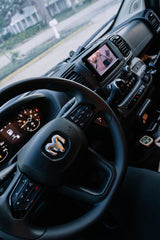Inside a modern RV rental van: steering wheel with Ram logo, dashboard, and infotainment screen displaying a camera view.