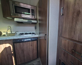 A well-equipped kitchen inside an RV rental, featuring a microwave, sink, two-burner stove, and compact refrigerator.