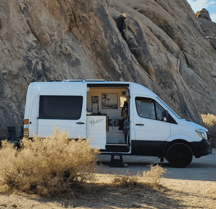 White camper van RV rental parked in a rocky desert landscape. Side door open, revealing a cozy interior for outdoor adventures.