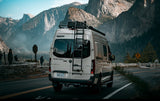 Epic rv rental adventure: A Winnebago Revel camper van pauses at a scenic mountain overlook with majestic peaks.