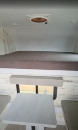 This rv rental features a compact interior with a raised sleeping area, light dining table, and ceiling vent.
