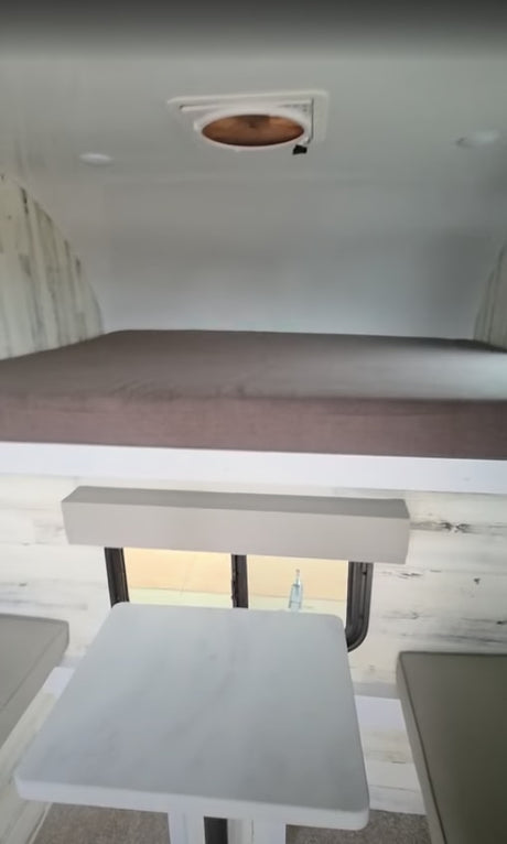 This rv rental features a compact interior with a raised sleeping area, light dining table, and ceiling vent.