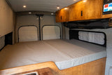 Cozy RV rental bed setup with wooden cabinets and soft lighting, ideal for camper van adventures.