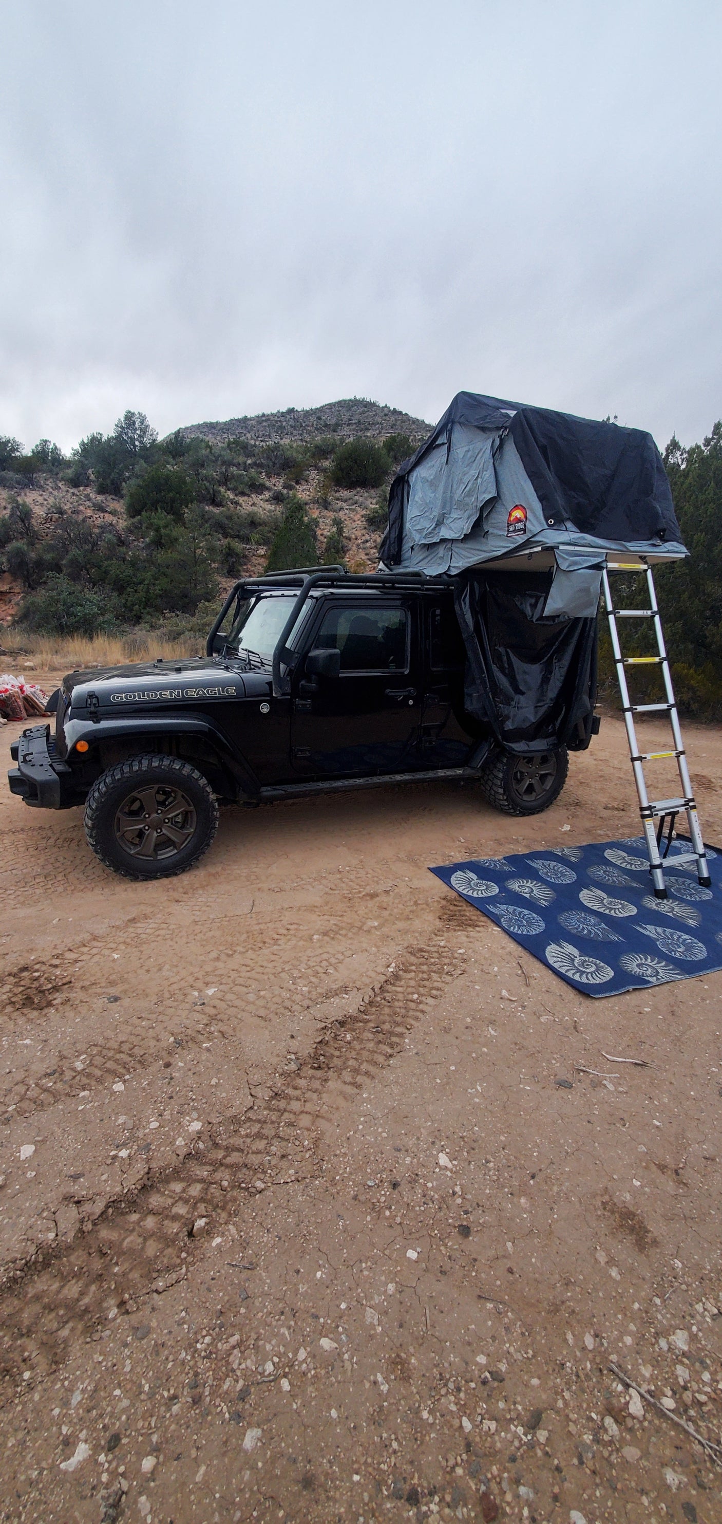 Black Jeep Wrangler with deployed roof-top tent & annex, a rugged RV rental for off-grid camping adventure.