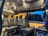 Inside a custom RV rental camper van, showing comfortable passenger seating, overhead storage, and a raised bed.