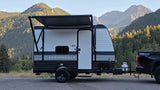 This Springdale travel trailer rv rental, hitched to a pickup truck, is parked amidst majestic mountains, ready for outdoor adventures.