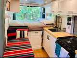 Modern RV rental interior: cozy bed, full kitchen, and colorful bench seating, ideal for travel.