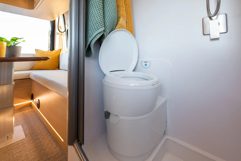 Compact RV rental interior featuring a Thetford portable toilet and shower, with a glimpse of the cozy living area. — photo 3