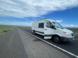 A white Sprinter camper van on a long, remote road under a big sky. An RV rental ready for adventure!
