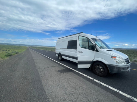 A white Sprinter camper van on a long, remote road under a big sky. An RV rental ready for adventure!