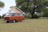 Orange pop-top VW camper van, ideal for RV rental adventures, parked in a grassy field with trees.