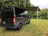 Gray camper van with an extended awning, parked on grass in a lush setting. Perfect for an RV rental adventure!