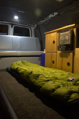 Cozy RV rental interior shows a green sleeping bag on a carpeted platform, heater, and bench seat. Ready for camping.