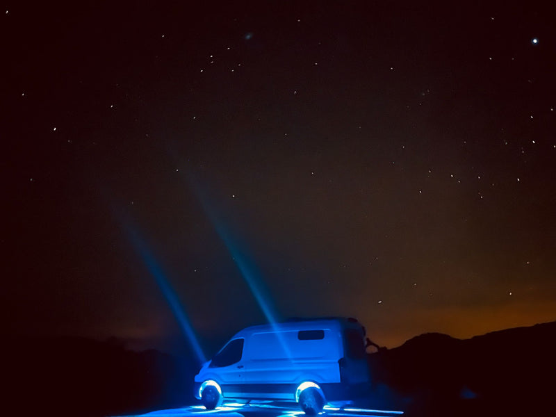  offering a beautiful waterfront view for a memorable vacation.|This white RV rental van enjoys a clear day above a cloud inversion from a dirt mountain road with bright sun.|White rv rental van parked on sandy coast by rocky ocean. Open door reveals interior. Angle Parking sign visible for travelers.|White Ford Transit camper van facing a brilliant waterfront sunset. Consider this RV rental for your scenic adventure!|White RV rental van at a beach sunset. Enjoy beach camping and road trip adventures with  — photo 13