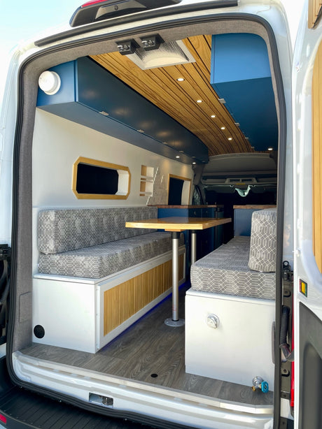 Step into this inviting rv rental! A custom camper van interior with a dining table, cozy benches, and warm wood accents.