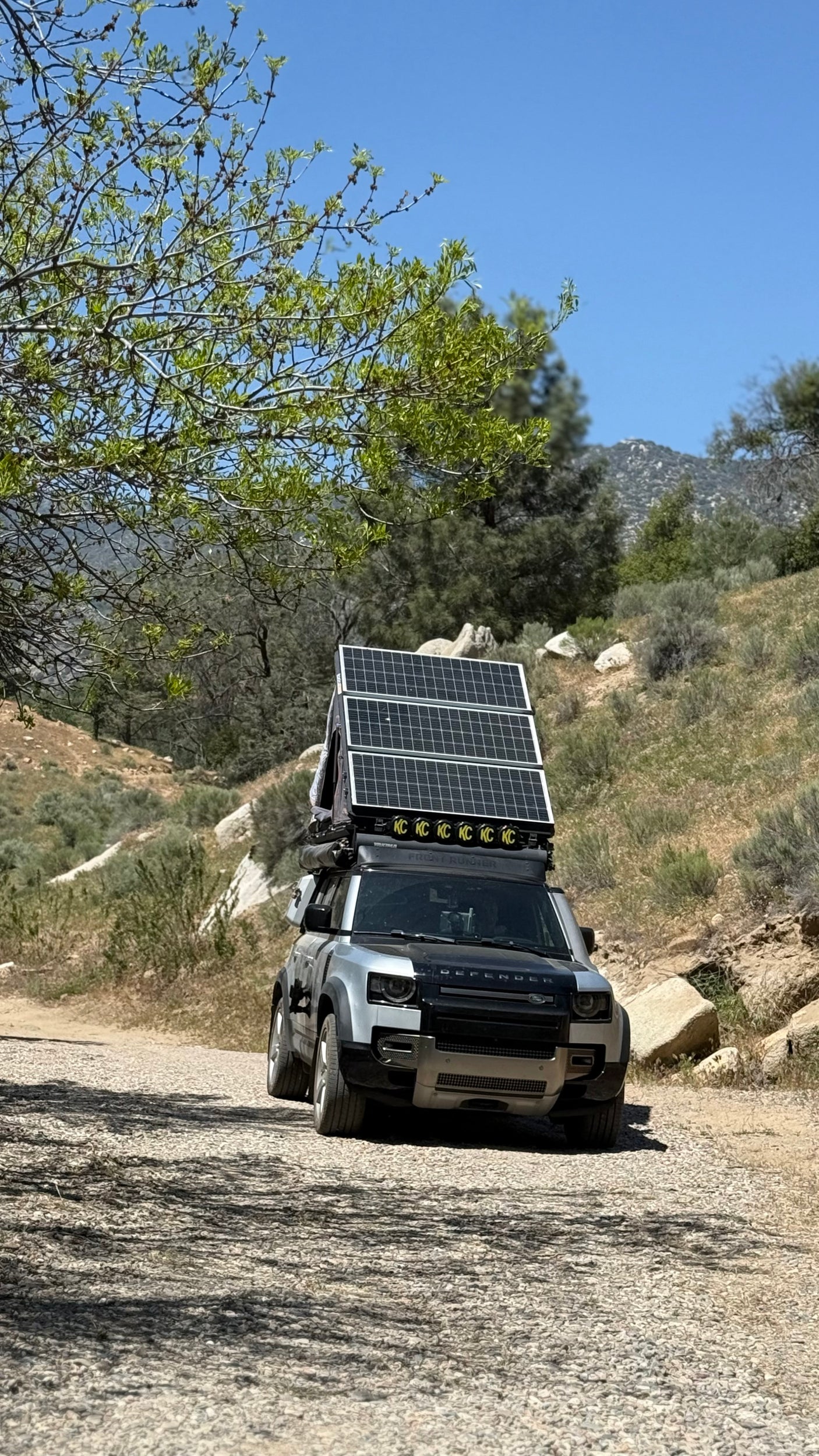 An overland-equipped Land Rover Defender, fitted with solar panels & rooftop tent, on a dirt road. Perfect for adventure, like an RV rental for the wild.