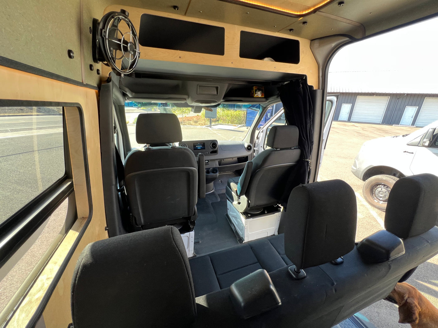 Inside an RV rental, showing versatile passenger seating, swivel front seats, custom overhead storage, and a fan.