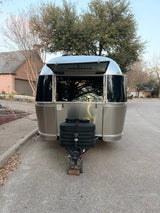 This silver Airstream travel trailer with an open hatch, revealing its logo, is parked and ready for your RV rental adventure.