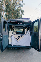 Inside a grey rv rental camper van: open rear doors reveal a cozy bed, cushions, and built-in amenities. Ready for adventure.