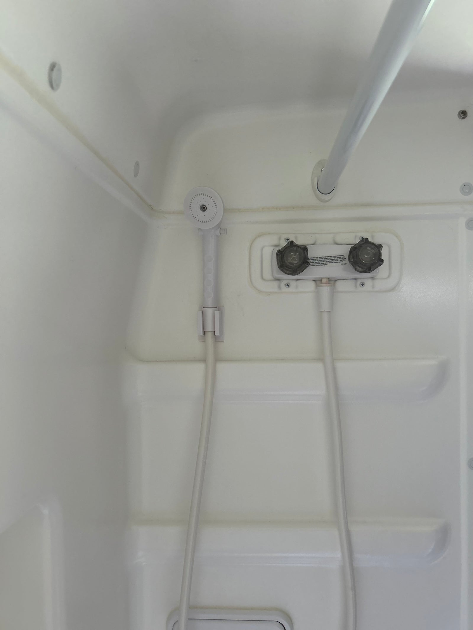 Compact white shower in an RV rental, with a hand-held shower head, faucet controls, and a grab bar.