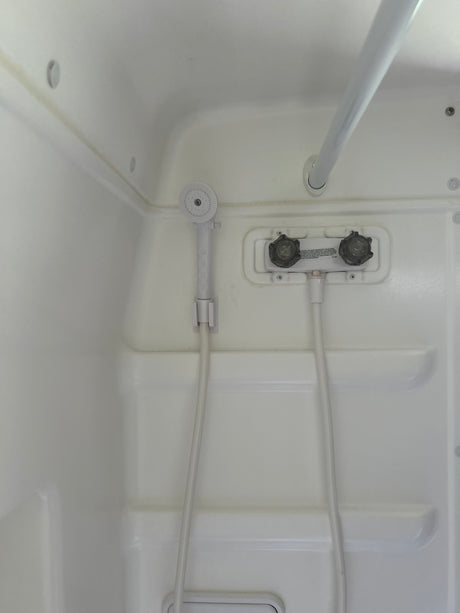 Compact white shower in an RV rental, with a hand-held shower head, faucet controls, and a grab bar.
