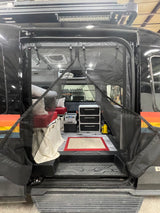 Interior view of a customized RV rental, showing a bed, storage drawers, fridge, and protective bug screen.
