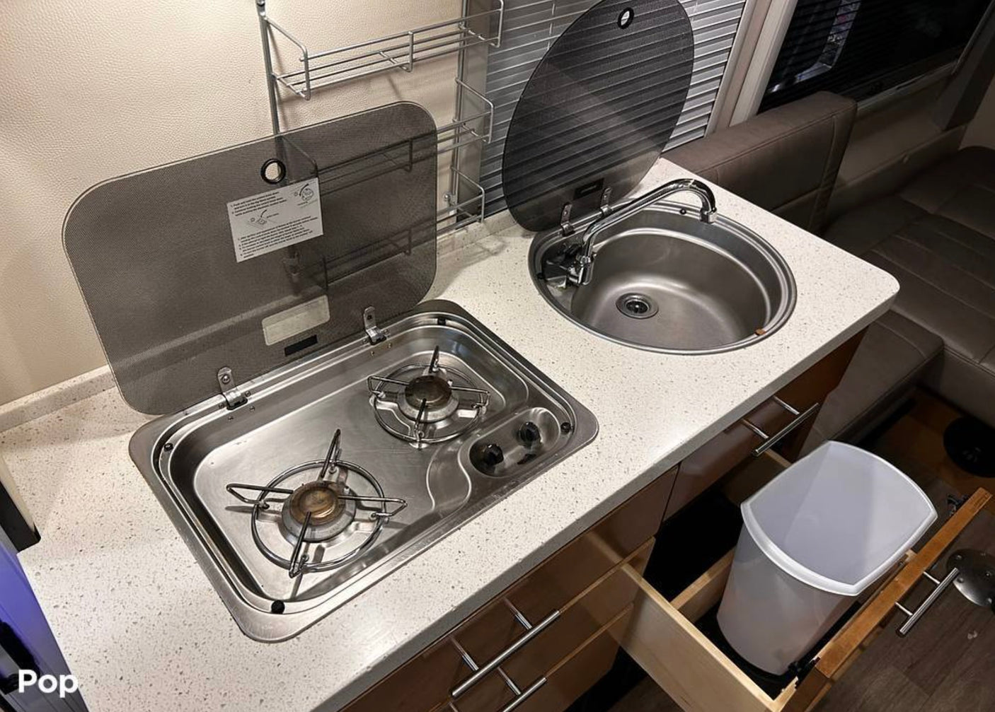 RV rental kitchen: 2-burner stove, sink, white countertop, and a convenient pull-out trash bin.