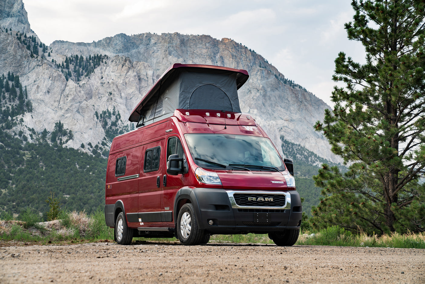 This red pop-top camper van for rv rental is parked on a scenic dirt road amidst majestic mountains.