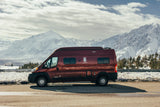 Red Winnebago Solis RV rental parked against a backdrop of majestic snow-covered mountains. Ideal for scenic road trips.