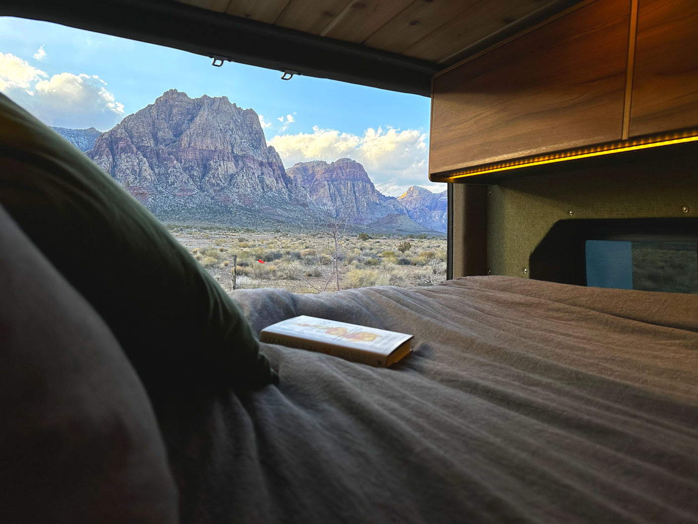 Enjoying a stunning desert mountain landscape from a cozy RV rental bed with a book. Perfect for serene travel & relaxation.