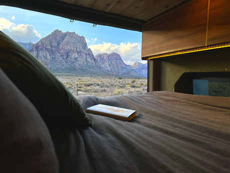 Enjoying a stunning desert mountain landscape from a cozy RV rental bed with a book. Perfect for serene travel & relaxation.