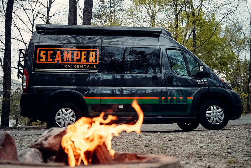 Dark gray Scamper RV rental van parked outdoors with a campfire in the foreground, surrounded by trees. — photo 15