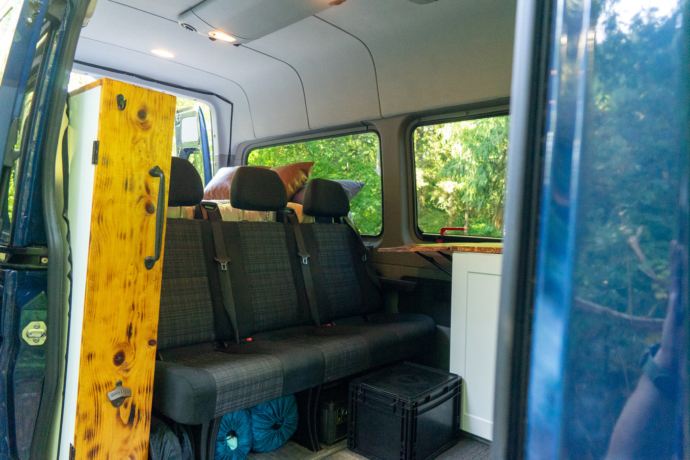 Inside a comfortable rv rental: rear seating, custom wood paneling with bottle opener, and kitchenette area for road trips.