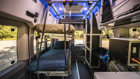 Inside an RV rental: a modular camper van interior with stacked bunk beds, smart storage, and vivid blue ambient lighting.
