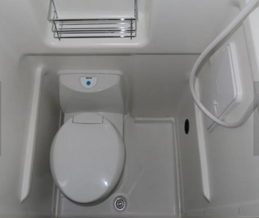 Compact white RV rental bathroom with a toilet, shower hose, and chrome shelf, ready for your trip.