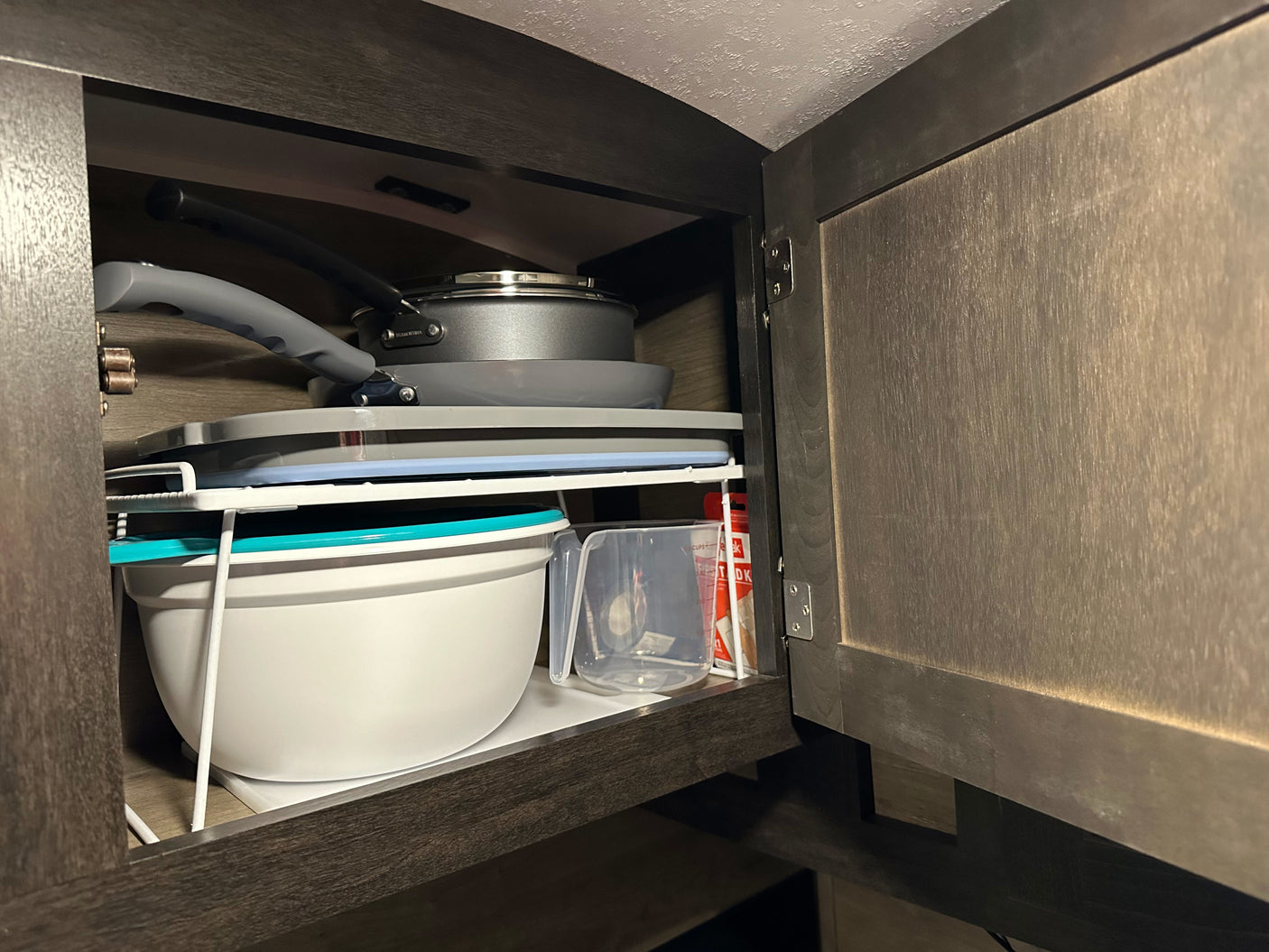 Organized kitchen cabinet in an RV rental, featuring stacked cookware, bowls, and measuring cups for efficient space.