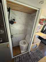 Compact rv rental wet bath featuring a shower, composting toilet, and elegant marble-look tiles. Perfect for van life.