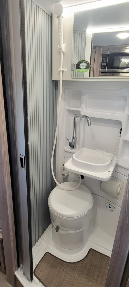 Compact RV rental wet bath with a toilet, fold-down sink, and a shower head on a hose. Perfect for road trip adventures.