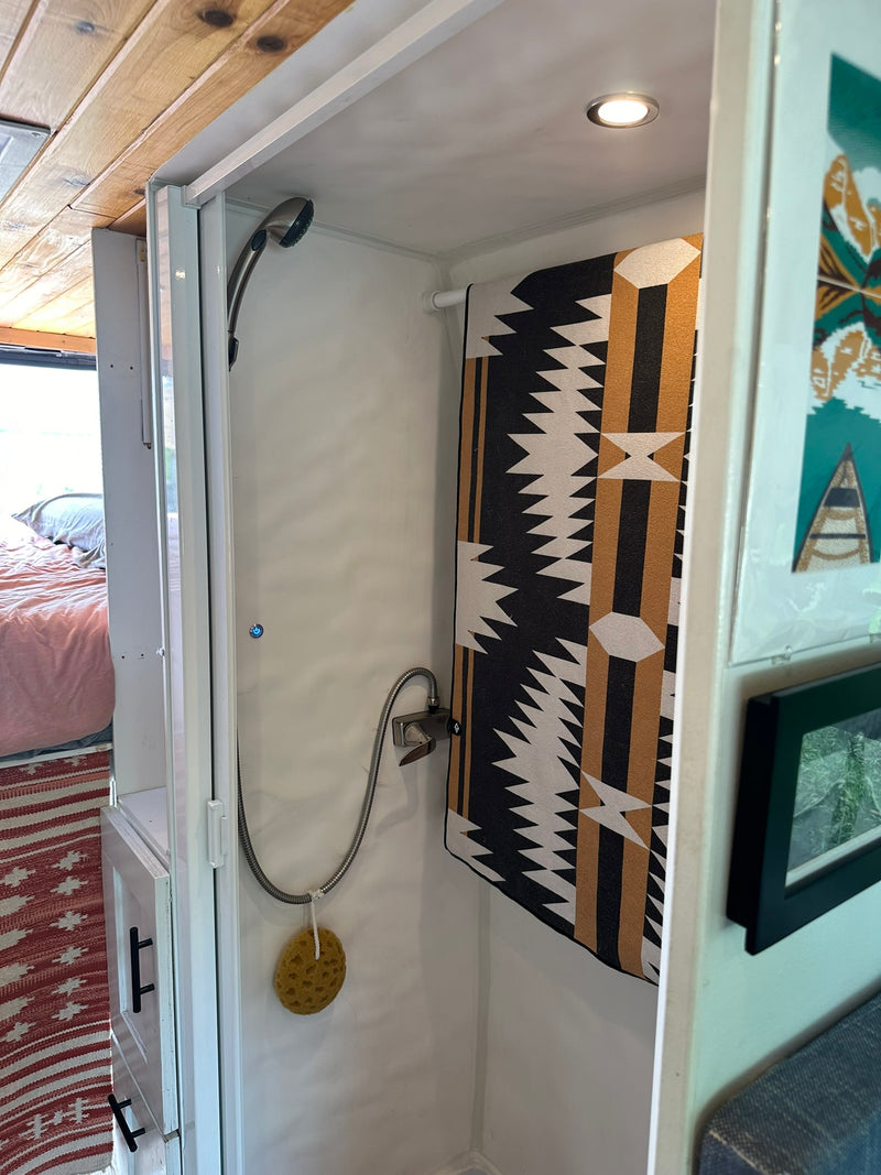 RV rental's compact shower stall with modern shower head, geometric towel, natural sponge, and wood ceiling visible. — photo 7