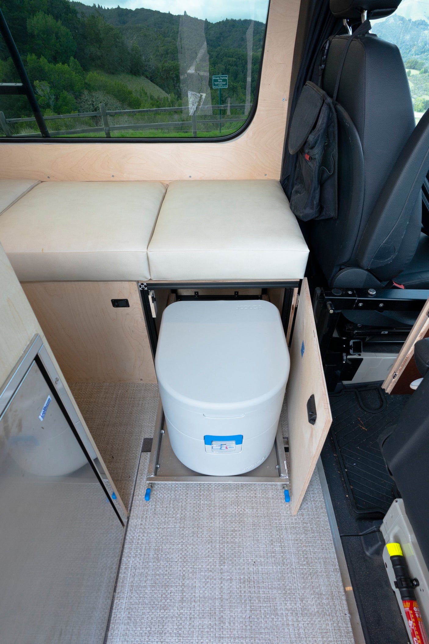 Explore this RV rental's compact interior: pull-out SCOLGA toilet, seating, fridge, & scenic window view.
