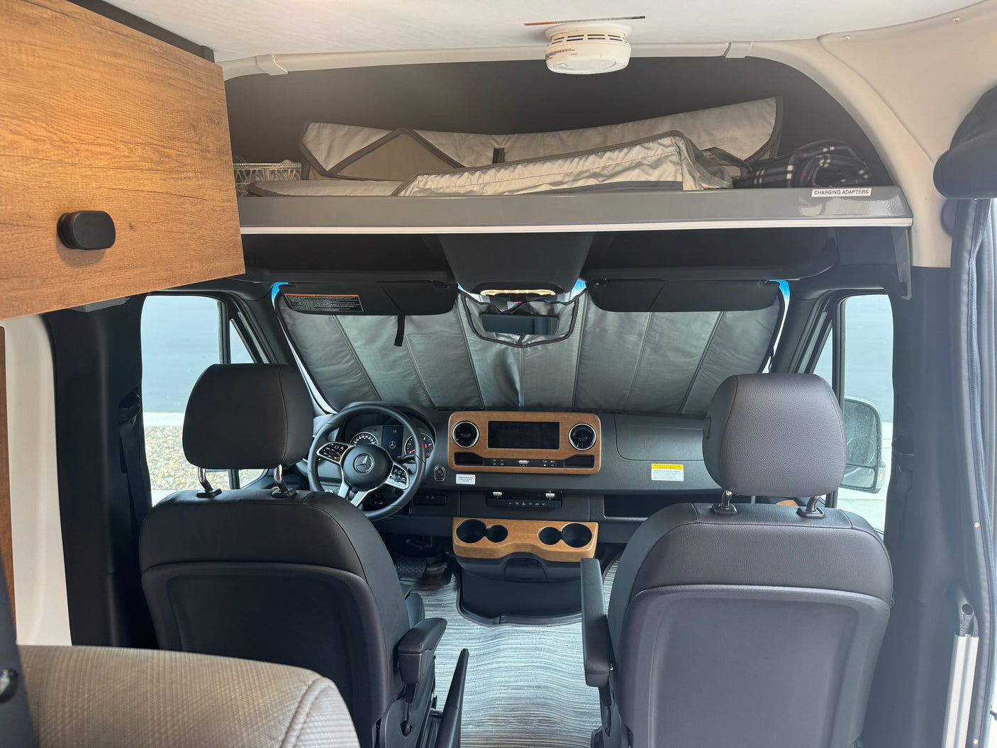 RV rental: view into the front cabin with Mercedes dashboard, steering wheel, sunshade, and overhead storage/bed.