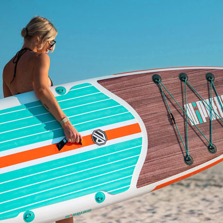 Woman carries a vibrant striped paddleboard on a sunny beach, ideal for an RV rental adventure.