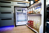 View inside a clean, organized refrigerator in an RV rental, featuring drinks and snacks, beside modern cabinetry.