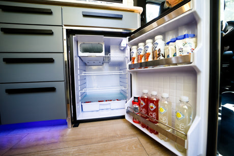 View inside a clean, organized refrigerator in an RV rental, featuring drinks and snacks, beside modern cabinetry.