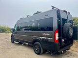 Dark grey Ethos overland camper van, equipped for off-road rv rental. Features roof rack & rear gear carrier.